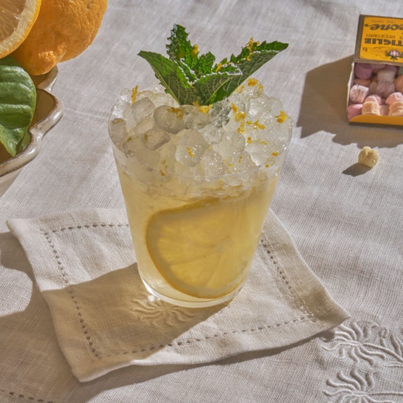 Short  yellow cocktail with ice, a lemon slice and mint garnish