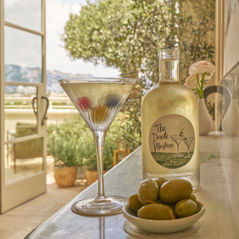 A martini cocktail placed upon the bar of the rooftop Dante, with olives at the bottom and a bottled cocktail next to it