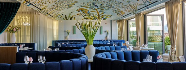 Dark blue booths surrounding tables with small pink roses on them, on the rooftop bar Dante with a ceiling mural above