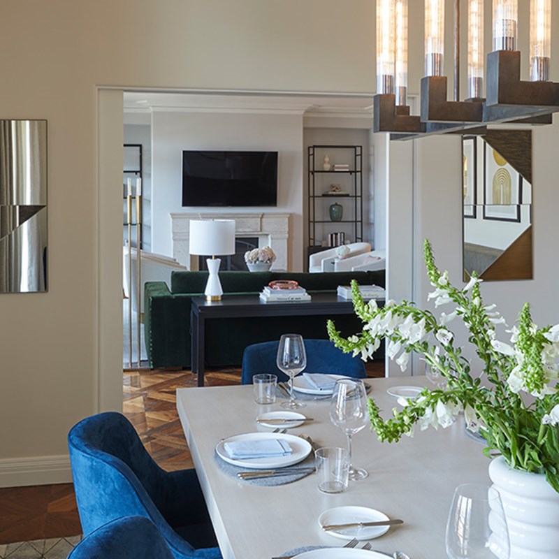 Edge of dining tables and blue dining chairs looking onto living room area with wall TV in The Residence