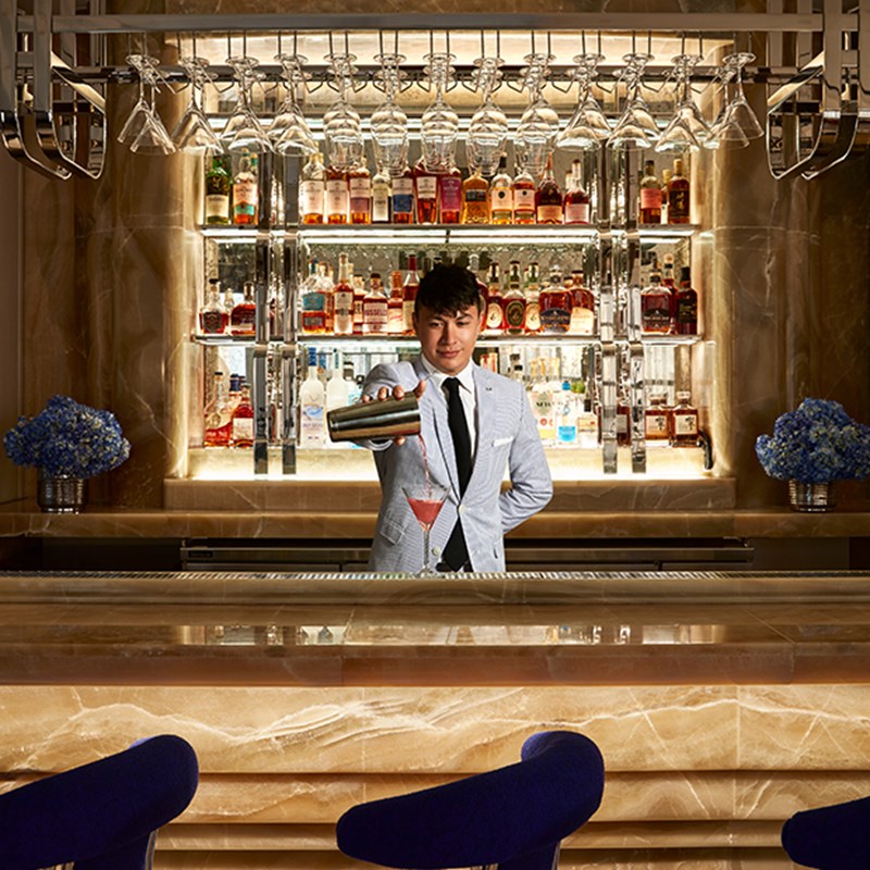 Head mixologist pouring drink drink standing in front of the bar